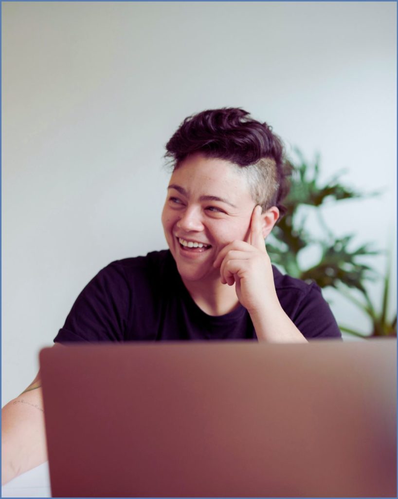 young adult with brown hair shaved on the side with a laptop in front of them and smiling